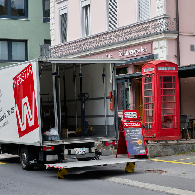 View of a narrow city street where Removal Company Kennington is engaged in a home relocation task, featuring two white moving vans parked partially on the pavement with the branding 'uniserve' and 'B
