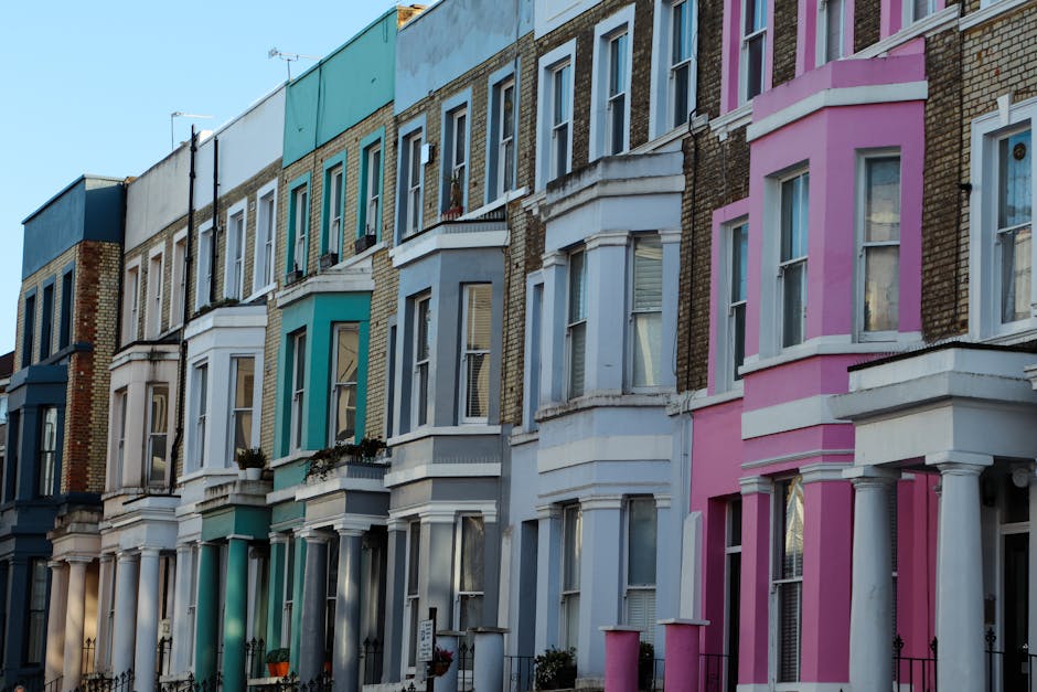 Exterior view of a row of Victorian terraced houses in Kennington, with each building featuring distinct pastel colour facades including shades of blue, green, white, and pink. The houses have bay win