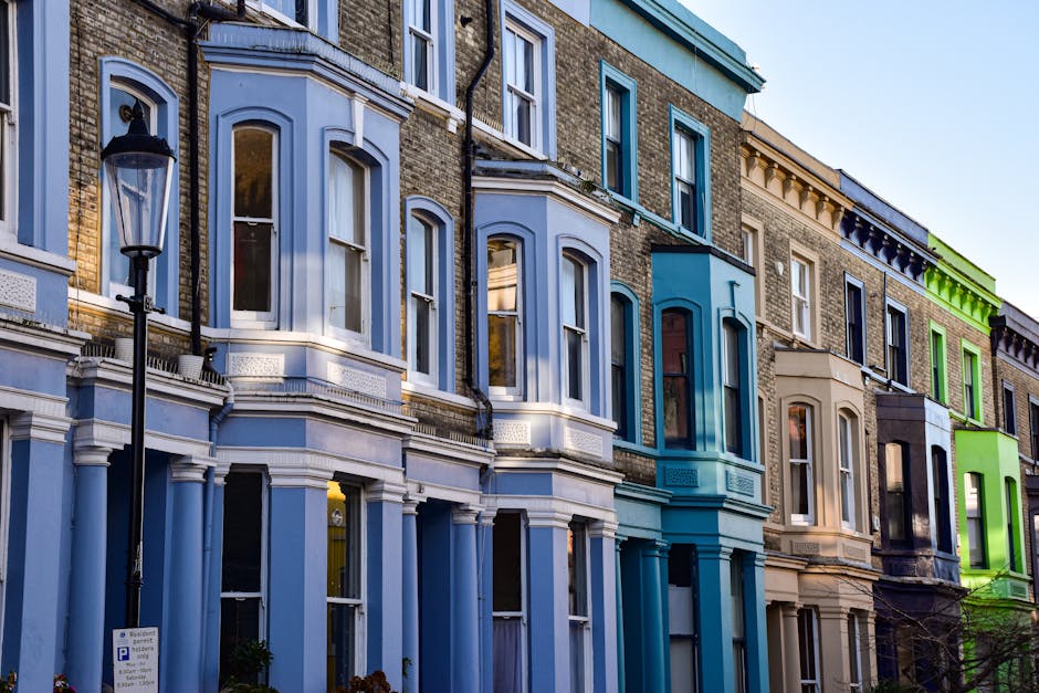 Exterior view of a row of Victorian terraced houses in Kennington, with each building featuring distinct pastel colour facades including shades of blue, green, white, and pink. The houses have bay win